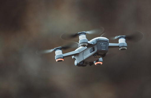 A grey drone flies outdoors.